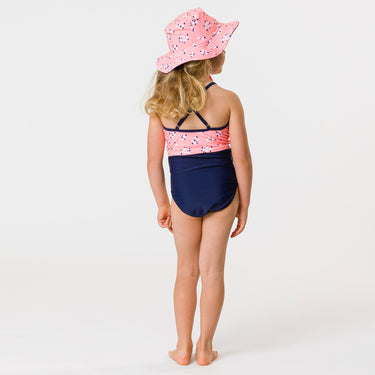 Girl wearing ditsy coral sunsuit and matching sunhat.