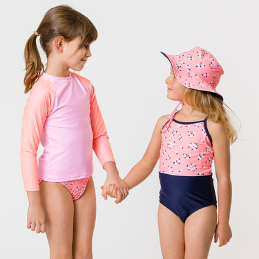 Two girls holding hands wearing Snapper Rock swimsuits.