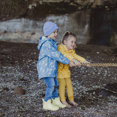 A boy and girl wearing Snapper Rock raincoats playing at beach.