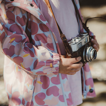 Close up of girl holding camera, wearing pink Apple Love raincoat.