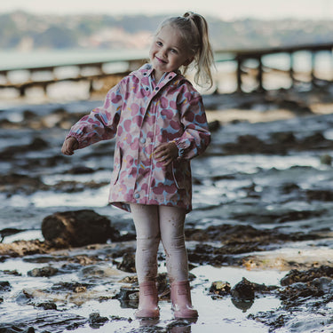 Girl playing at beach wearing pink raincoat.