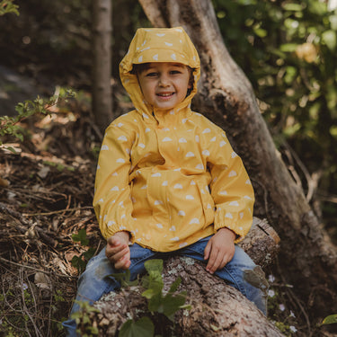 Boy sitting on tree branch wearing Snapper Rock yellow Sun Cloud raincoat.