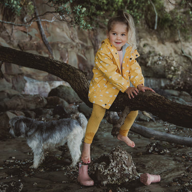 Girl sitting on tree branch at beach, wearing yellow waterproof raincoat.