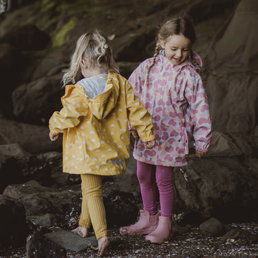 Two girls exploring rocks at beach, both are wearing Snapper Rock Adventurewear raincoats.