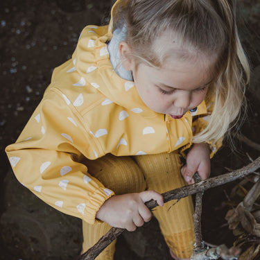 Girl rubbing sticks together, wearing Sun Cloud yellow kids raincoat.